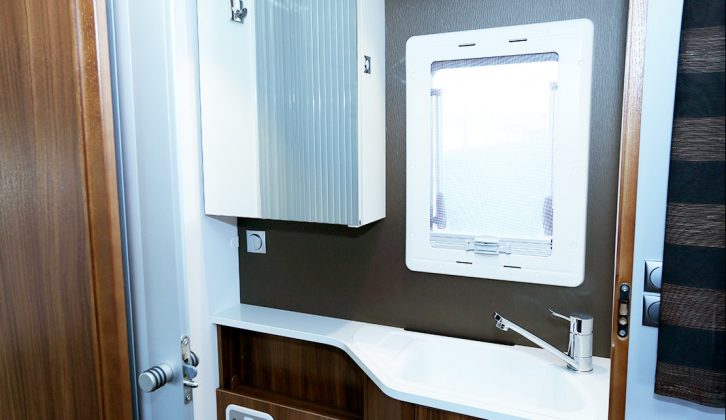 This motorhome has a split washroom, with a sink, vanity unit, cupboard and swivelling toilet on the offside, a sliding tambour door provided for privacy