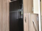 The tall, slimline fridge/freezer is opposite the main kitchen, with a microwave above; the adjacent narrow cupboard is the dedicated storage space for the dining table