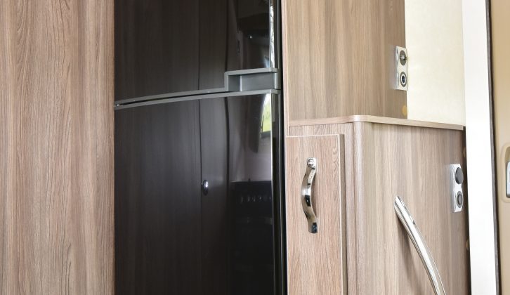 The tall, slimline fridge/freezer is opposite the main kitchen, with a microwave above; the adjacent narrow cupboard is the dedicated storage space for the dining table