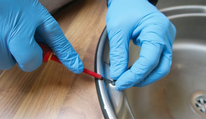 The first step in removing the kitchen sink is to take off the screw caps, using a flat-blade screwdriver