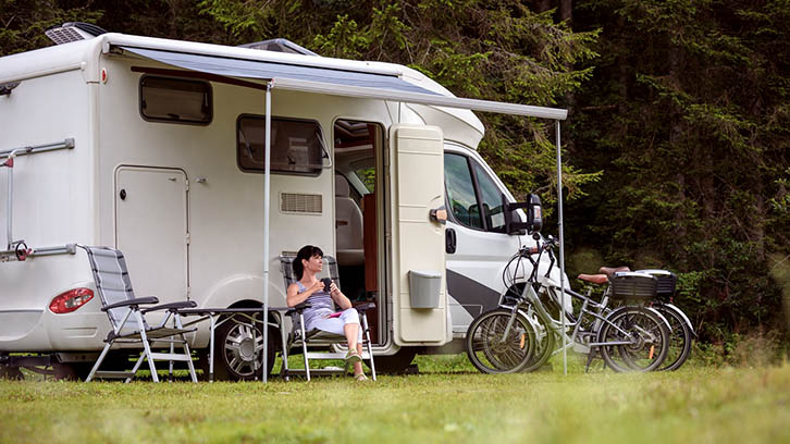Woman sitting by a motorhome, with two bikes parked nearby.