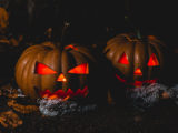 2 pumpkins on a dark night with a lit candle illuminating each one