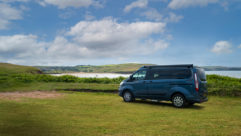 Exterior shot of the campervan, parked on grass by water