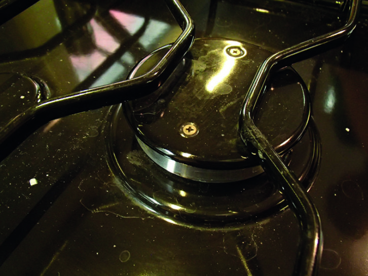 Gas burner under the trivet, showing two screws allowing access for cleaning and checking