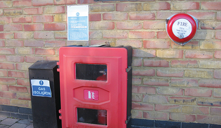 A fire alarm and fire extinguisher in place on a brick wall