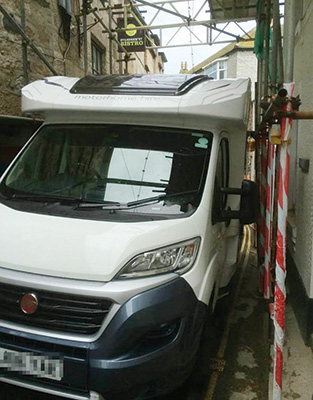 A motorhome driving down a narrow street with scaffolding on either side