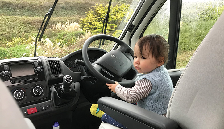 A toddler sitting in the driver's seat of a parked motorhome