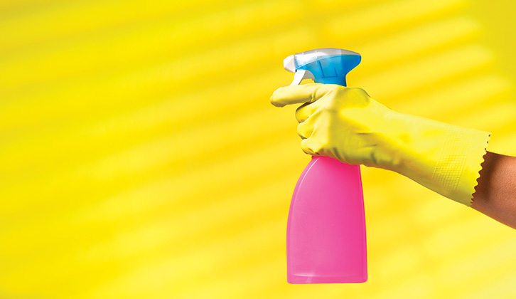A spray bottle full of pink cleaner held by a hand wearing a yellow rubber glove