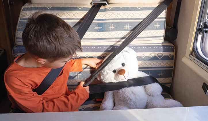 A child with his teddy bear next to him, both wearing seatbelts