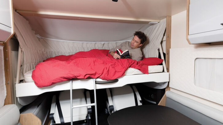 Man reading in an over-cab bed in a motorhome.