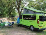 A campervan pitched up with folding tables and chairs set up