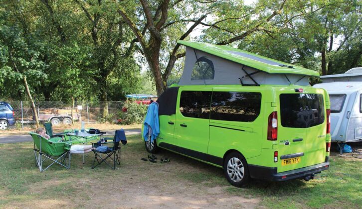 A campervan pitched up with folding tables and chairs set up