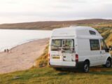 A campervan with a bike rack on its rear door parked up by the coast