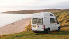 A campervan with a bike rack on its rear door parked up by the coast