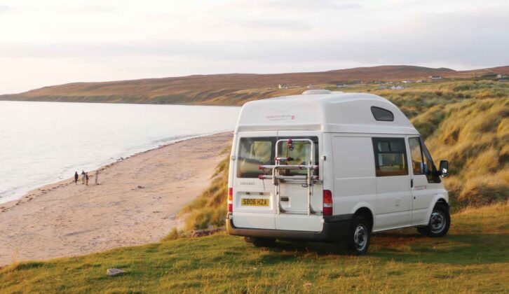 A campervan with a bike rack on its rear door parked up by the coast