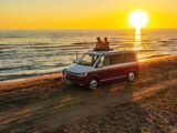 Couple sitting together on roof of campervan at beach while enjoying sunset