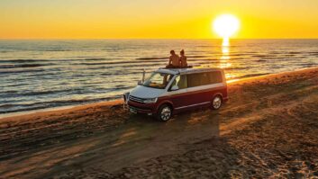 Couple sitting together on roof of campervan at beach while enjoying sunset