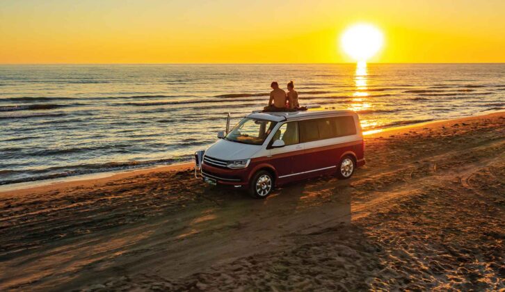 Couple sitting together on roof of campervan at beach while enjoying sunset
