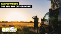 A person taking a photo of a sunset with a campervan in the background