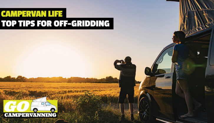 A person taking a photo of a sunset with a campervan in the background