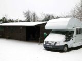 An overcab motorhome parked up with snow on its bonnet and roof