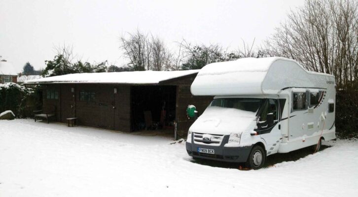 An overcab motorhome parked up with snow on its bonnet and roof