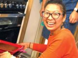A woman smiling at the camera as she puts a tray in the cooker