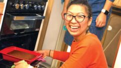 A woman smiling at the camera as she puts a tray in the cooker