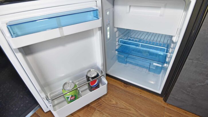 A fridge with a couple of cans of fizzy drink in it