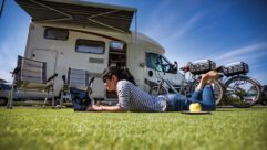 A woman laying on the grass on her laptop while her motorhome is in the background