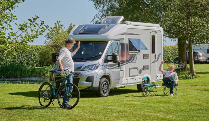 Peter with a bike waving to someone relaxing outside their motorhome