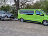 A car being towed on the trailer of a campervan