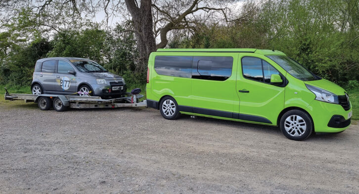 A car being towed on the trailer of a campervan