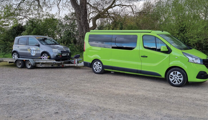 A car being towed on the trailer of a campervan