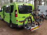 A campervan parked up in a wooded area with a cycle rack attached