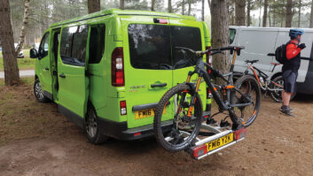 A campervan parked up in a wooded area with a cycle rack attached