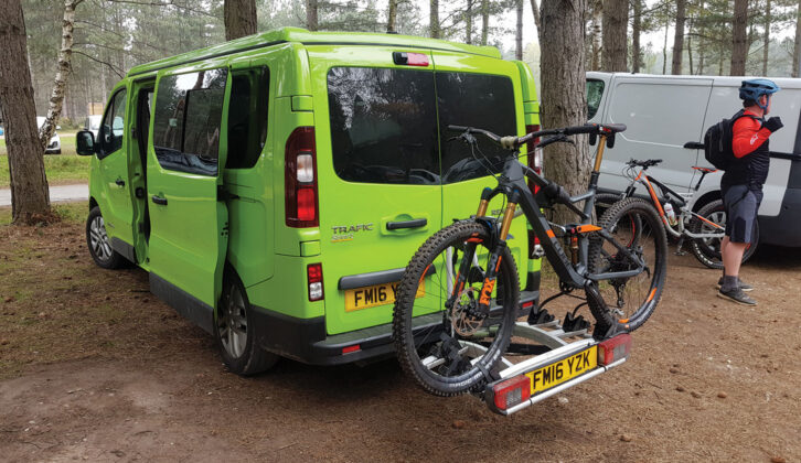 A campervan parked up in a wooded area with a cycle rack attached