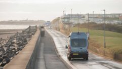 A campervan being driven down a road by the seafront