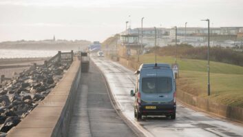 A campervan being driven down a road by the seafront