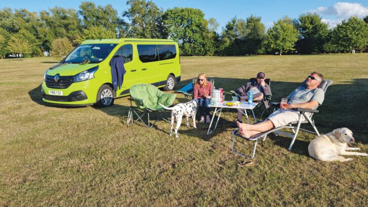 A family relaxing by their campervan pitch with their dogs