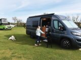 A dog in the shade of a pitched up campervan